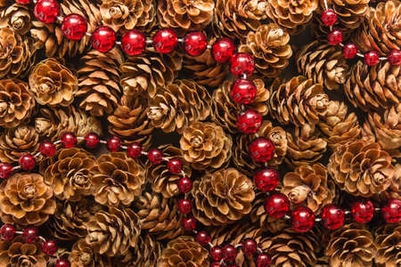 Festive Christmas background random pattern with many wooden pine cones and red balls garland.