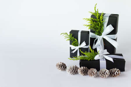 Pile of winter Christmas New Year presents wrapped in black paper with white satin ribbon and bow with evergreen branch and white wooden pine cones. Photo with copy blank empty space.の写真素材