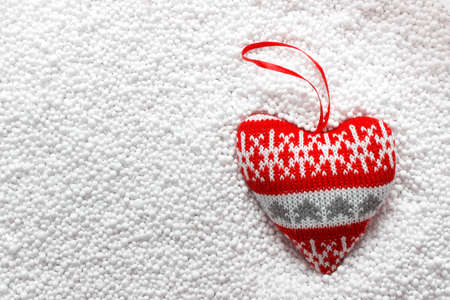 Winter holiday toy decor heart with Christmas knitted ornament laying on plastic bubble white filling representing snow.の写真素材