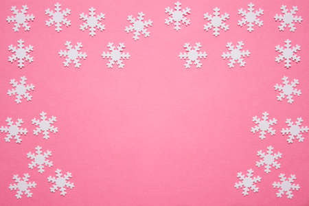 Winter Chrstimas composition made of many small white snowflkes arranged on pink backgound with copy...