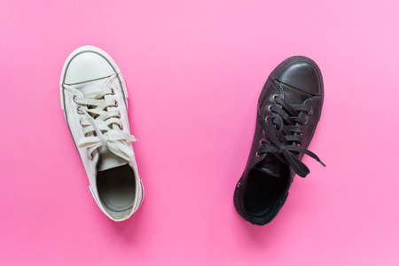 Two rubber gum sneakers shoes white and black on pink background. Concept of similarity and difference, white and black steps.の写真素材