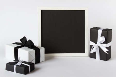Presentation photo picture frame with black empty blank paper and three gift present boxes on white background.の写真素材