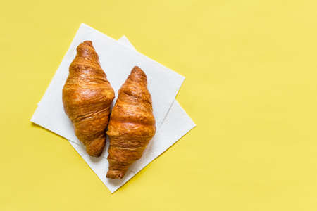 Two sweet breakfast croissants on white paper napkin on vibrant yellow background. Photo with copy blank space.の写真素材
