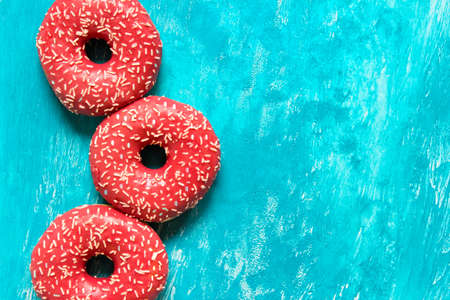 Three donuts with pink glaze and sugar sprinkles on blue background. Photo with copy blank space.の写真素材