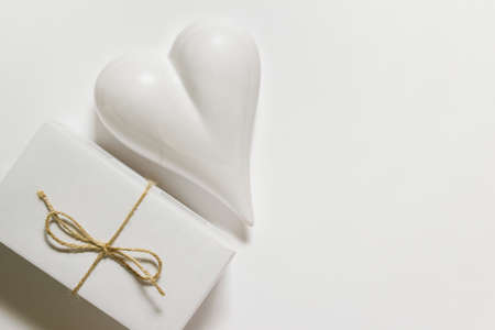 Valentine's, Mother's, Father's day greeting card with porcelain heart and present wrapped in white paper with a bow of rough rope packthread on white background. Photo with copy blank space.の写真素材