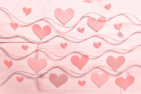 Valentine day pattern with hearts arranged on wooden background with wavy rope tinted with pink...