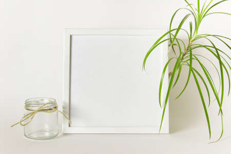 Mockup with empty blank square frame, green plant and empty glass jar with rough packthread rope on...
