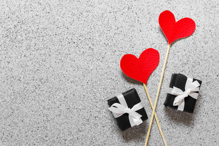 Valentine day celebration greeting card with two red hearts on wooden sticks and two little presents with white bows on stone texture background.の写真素材