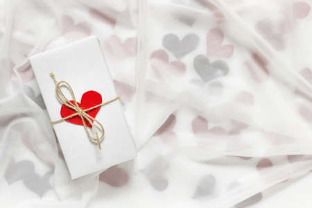 Valentine day gift present with red heart and packthread bow on background of surface with red...