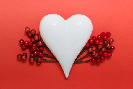 Valentine day greeting card with white porcelain heart and decorative branches with red berries on red background.の写真素材