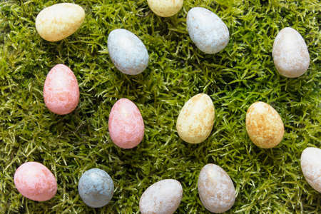Many colorful decorative Easter eggs randomly arranged on green moss.