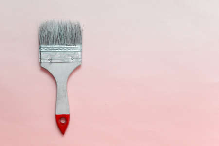 Single cheap paint brush with red tip and synthetic bristles on pink background. Photo with copy...