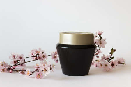 Packaging template mockup with black shiny jar and branch twig of Sakura plant tree on white background.の写真素材