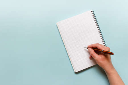 Hand writing in spiral notebook with metallic pen on blue background. Photo with copy blank space.