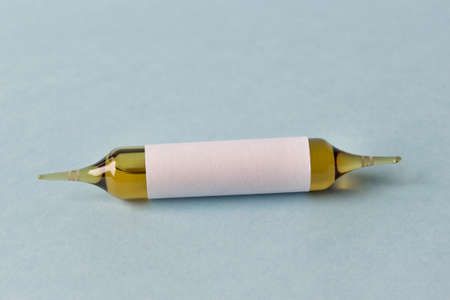 Single dark glass air sealed ampule with white paper cover on blue background.の写真素材