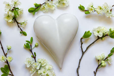 Greeting card with white porcelain heart decorated with blooming twigs branches of spring apple tree on white background.の写真素材