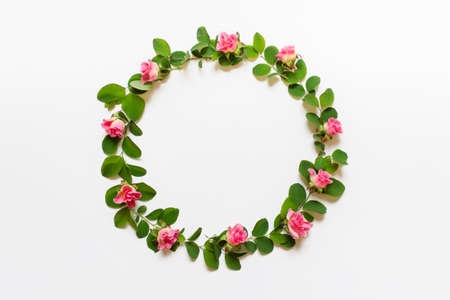 Round circular wreath with green plant branches and pink roses on white background.の写真素材