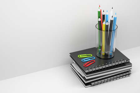 Pile of black spiral notebooks, paper pins and glass with colorful pencils standing on top. 3d...
