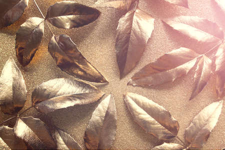 Abstract golden composition with golden leaves on golden sparkling glitter paper.