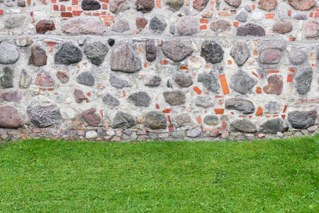 Background with combination of two textures - stone wall of historic building and green fresh trimmed grass.の写真素材