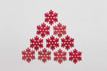 Red wooden craft snowflakes arranged as a triangle on white background.の写真素材