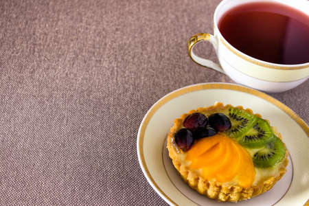 Sweet confectionery little cake on a plate with red tea. Photo with copy blank space.