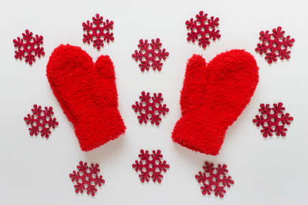 Red fluffy kids mittens with many red wooden snowflakes on white background.の写真素材