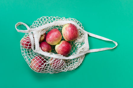 Organic apples in an opened biodegradable eco friendly string bag on green background.の写真素材