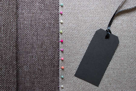 Sewing background with textured fabric and black paper label on satin rope.