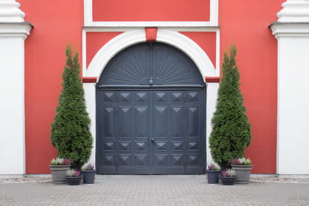 Entrance vintage medieval doors of historical building with symmetrical arrangement of potted...