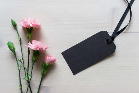 Mockup template with black blank empty clothes label with pink flowers on wooden background.の写真素材