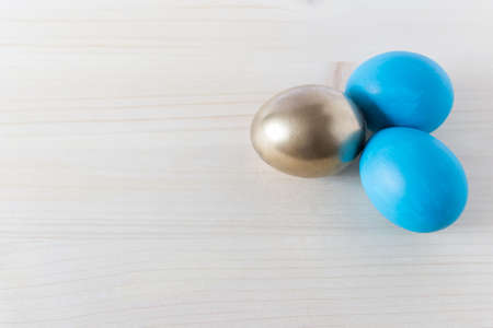 Simple minimalistic Easter background with blue and golden colored eggs on wooden background. Photo...