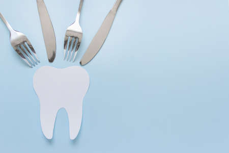 One large paper tooth with eating utencils forks and knifes on blue background. Photo with copy...