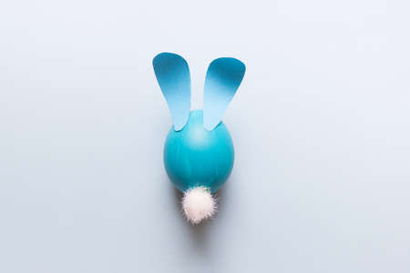 Easter composition with one cartoon stylized blue egg with paper ears and white fluffy tail on blue...