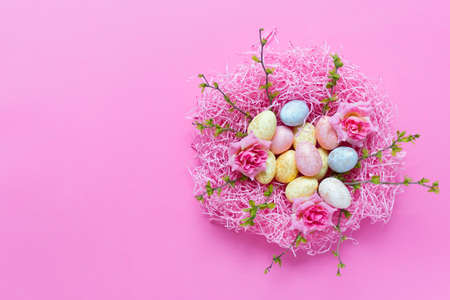 Easter composition with spring foliage branches and pink nest filled with small colorful eggs on pink background.の写真素材