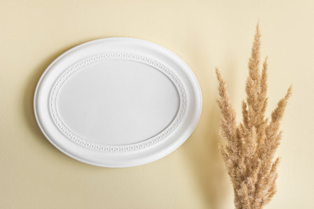Mockup template with blank oval photo image frame with blank space and yellow fluffy plants on the background of yellow wall.の写真素材
