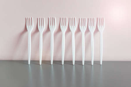 Many white plastic forks standing in row on gray reflective surface next to yellow wall.