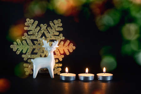 Christmas, New Year composition with three candles, white porcelain reindeer and golden snowflake on black background.の写真素材