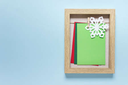 Christmas, New Year mockup template with wooden frame, white paper snowflake and colored blank cards on blue backgound. Photo with copy blank space.の写真素材
