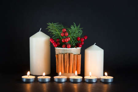 Christmas, New Year composition with white candles, cup with cinnamon decor, fir evergreen and red berries on black background.の写真素材