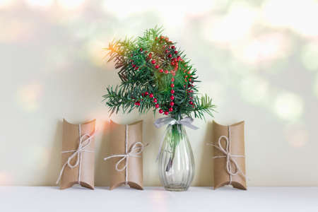 Christmas, New Year composition with craft paper boxes and glass vase with fir evergreen branch with red balls garland.の写真素材