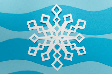 Christmas, New Year simple decor- hand carved paper snowflake on blue background.の写真素材