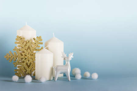 Christmas, New Year composition with three white candles, white porcelain reindeer, golden snowflake and white balls on blue yellow background. Photo with copy blank space.の写真素材