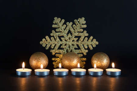 Christmas, New Year greeting card with golden large snowflake, three golden balls and burning candles on black background.の写真素材