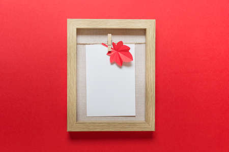 Simple mockup template with wooden A5 frame and red autumn paper maple leaf on red background.の写真素材