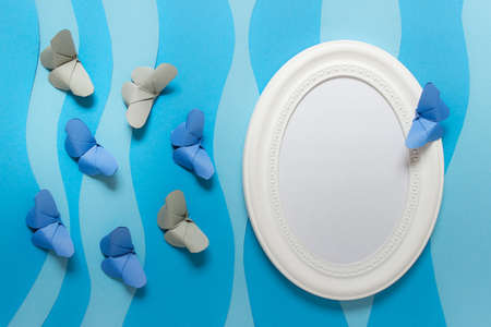 Mockup template with oval white frame with paper folded origami butterflies on blue paper layers.の写真素材