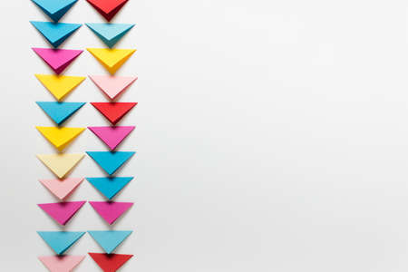 Simple background with many colorful folded paper triangles arranged in two columns. Image with white copy blank space.の写真素材