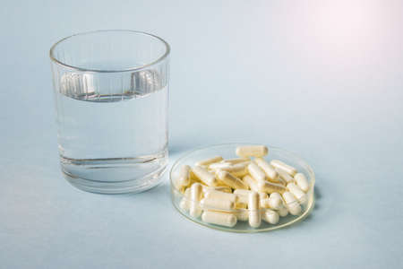 Medical illustration with glass of water and many white pills in Petri dish on blue background.の写真素材