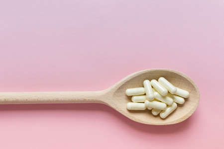 Medical illustration with wooden spoon filled with pills capsules, supplements on pink background....