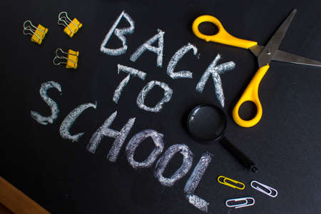 Inscription back to school. On a chalky black board. Handwritten. Stationery school accessories....